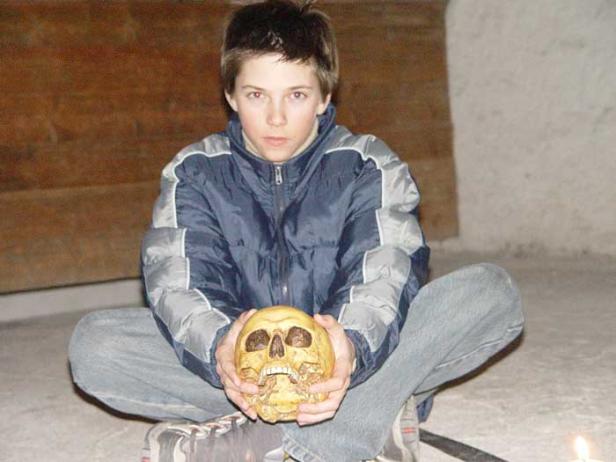 Ein junger Mann sitzt im Schneidersitz und hält einen Schädel in den Händen.