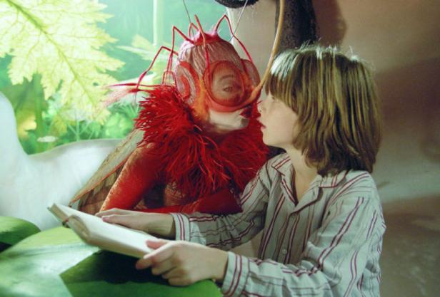 Ein Junge im Schlafanzug liest einem Wesen mit Insektenkopf aus einem Buch vor.