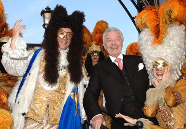 Ein Mann im Anzug posiert mit kostümierten Personen mit Masken und Perücken.