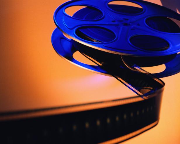Eine blaue Filmrolle mit einem aufgerollten Filmband vor einem orangefarbenen Hintergrund.
