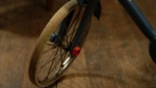 Das Vorderrad eines Fahrrads mit Schutzblech steht auf einem Holzboden.