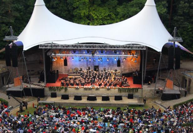 Ein Orchester spielt vor großem Publikum in einem Open-Air-Theater.