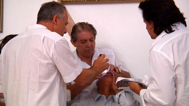 Ein Mann wird von zwei Ärzten untersucht, einer leuchtet ihm mit einer Lampe ins Auge.