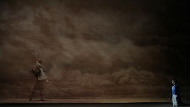 Auf einer Bühne tanzen ein Mann und eine Frau vor einem gemalten Hintergrund mit Wolken.