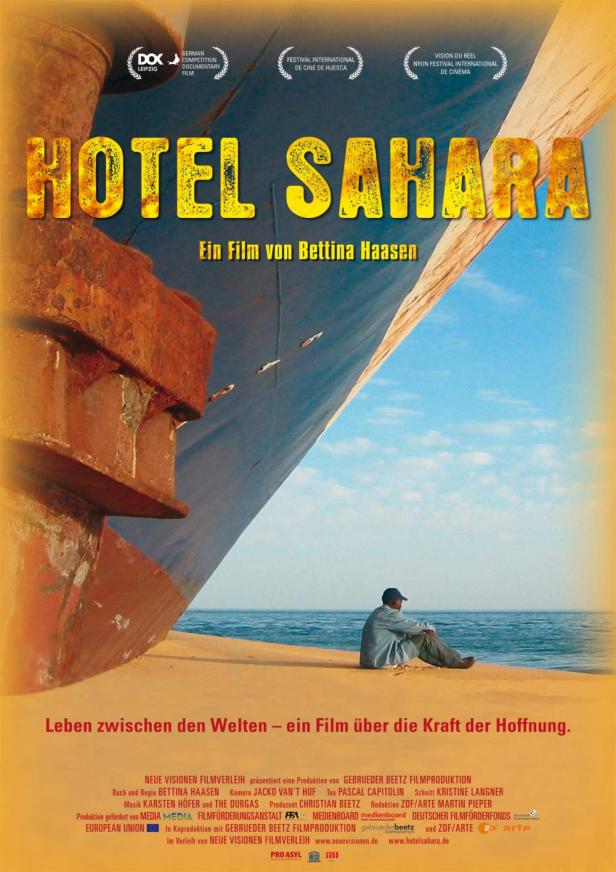 Das Filmplakat für „Hotel Sahara“ zeigt einen Mann vor einem großen Schiff.