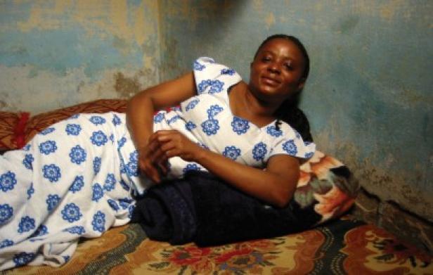 Eine Frau liegt in einem blau-weiß gemusterten Kleid auf einem Bett.