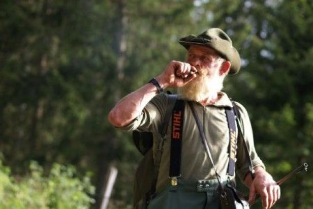 Ein Mann mit Hut und Bart pfeift in der Natur.