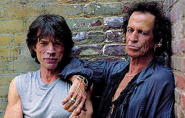 Mick Jagger und Keith Richards posieren vor einer Ziegelwand.