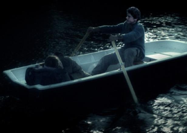 Ein junger Mann rudert ein Boot, in dem eine weitere Person liegt.
