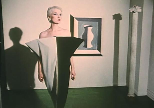 Eine Frau in einem schwarz-weißen Kleid posiert vor einem Gemälde und einer Säule.