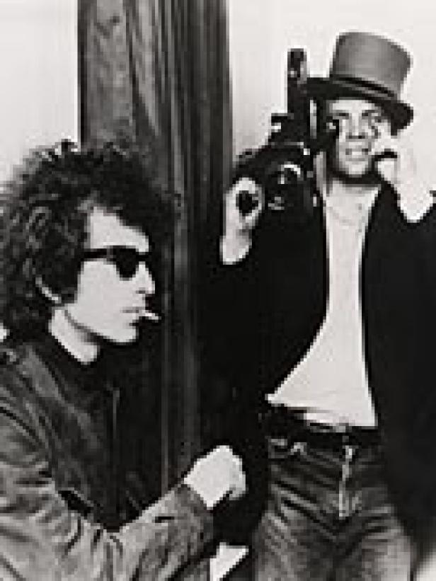Bob Dylan mit Sonnenbrille und ein Mann mit Zylinder und Kamera in Schwarzweiß.