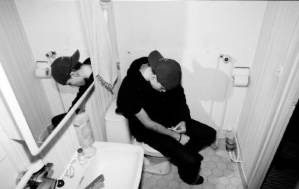 Eine Person sitzt erschöpft auf einer Toilette in einem Badezimmer.