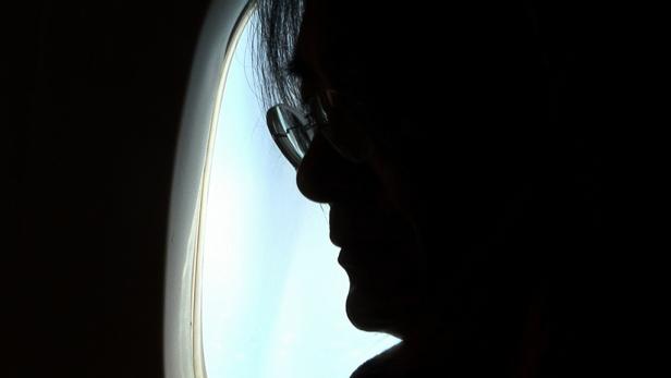 Die Silhouette eines Mannes mit Brille, der aus einem Flugzeugfenster schaut.