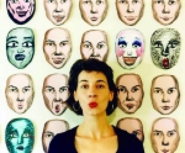 Eine Frau steht vor einer Wand mit bemalten Gesichtsmasken.