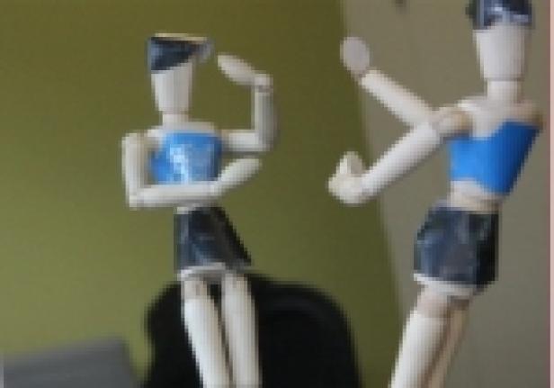 Zwei hölzerne Gliederpuppen, eine sitzend und eine stehend, posieren.