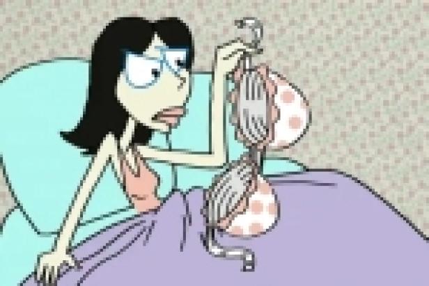 Eine Frau sitzt im Bett und hält einen BH mit rosa Punkten hoch.