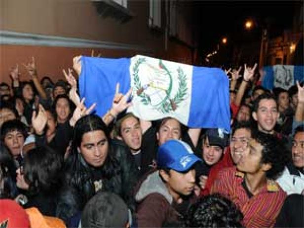 Eine Menschenmenge hält eine guatemaltekische Flagge hoch und jubelt.