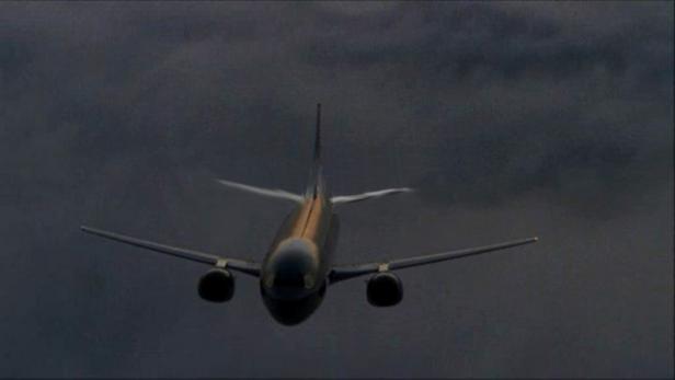 Ein Flugzeug fliegt vor einem dunklen, bewölkten Himmel.