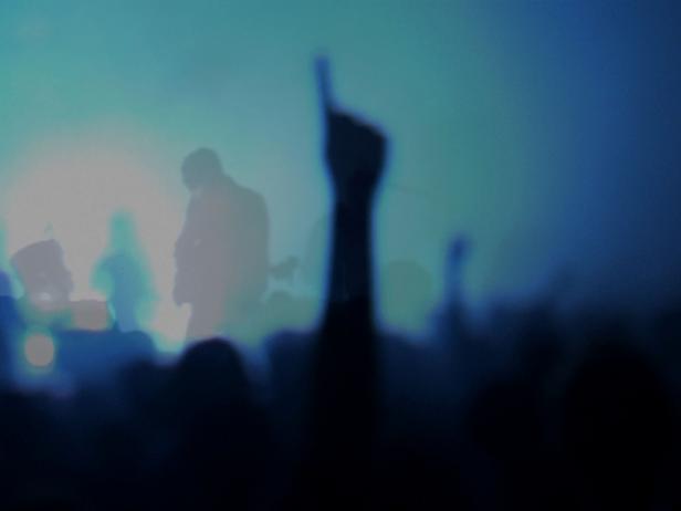 Eine Menschenmenge jubelt bei einem Konzert mit blauer Bühnenbeleuchtung.