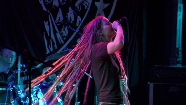 Eine Sängerin mit Dreadlocks tritt auf einer Bühne vor einem Schlagzeuger auf.