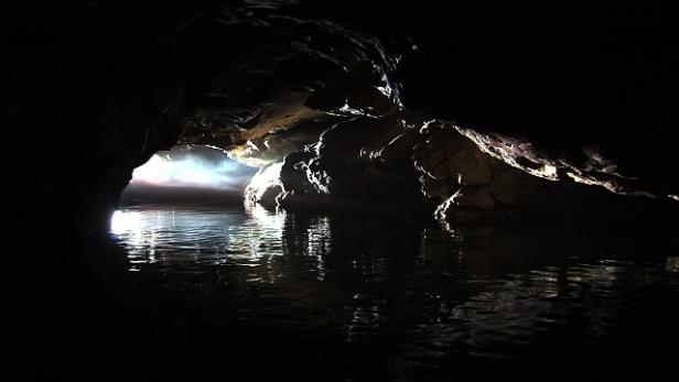 Ein unterirdischer See in einer dunklen Höhle mit einem hellen Ausgang.