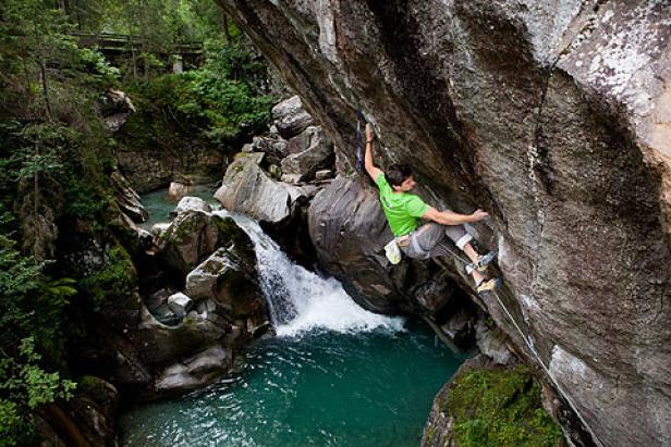 Ein Mann klettert an einer Felswand neben einem Wasserfall.