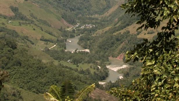 Blick auf ein Flusstal mit einem kleinen Dorf, umgeben von grünen Hügeln.