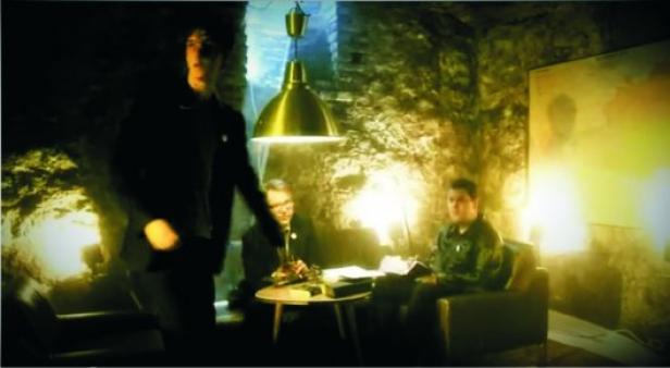 Drei Personen in einem spärlich beleuchteten Raum mit Steinhintergrund.