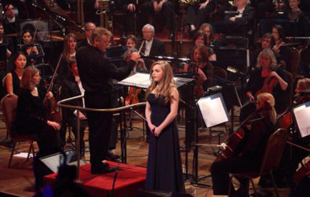 Eine junge Sängerin tritt mit einem Orchester auf einer Bühne auf.