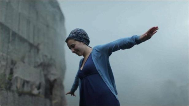 Eine Frau balanciert mit ausgestreckten Armen vor einer grauen Felswand im Nebel.