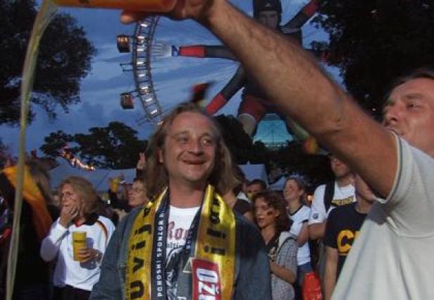 Ein Mann wird auf einem Festival mit Bier übergossen, im Hintergrund ein Riesenrad.