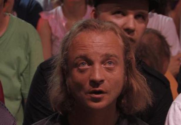 Ein Mann mit langen blonden Haaren schaut erwartungsvoll nach oben.