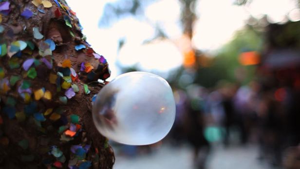 Ein verkleideter Mann mit Konfetti bläst eine riesige Seifenblase.