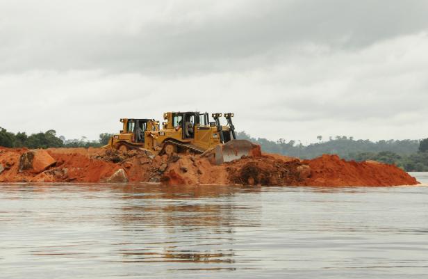 Zwei gelbe Bulldozer schieben Erde in einem Gewässer zusammen.