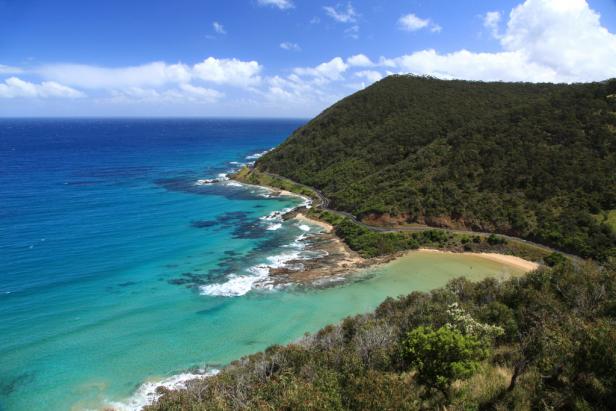 Die Küstenstraße schlängelt sich an einem bewaldeten Hügel entlang, mit Blick auf das türkisfarbene Meer.