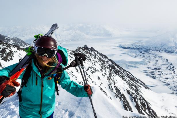 Eine Skifahrerin steigt mit Skiern auf dem Rücken einen schneebedeckten Berg hinauf.