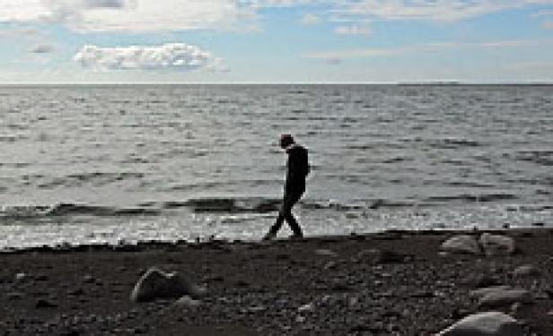 Eine Person geht am Strand entlang, das Meer im Hintergrund.