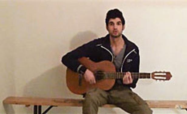 Ein junger Mann sitzt auf einer Bank und spielt Gitarre.