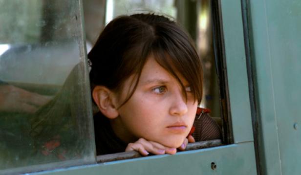 Ein junges Mädchen blickt aus dem Fenster eines grünen Fahrzeugs.