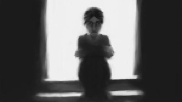 Eine Frau steht vor einem Fenster und verschränkt die Arme.