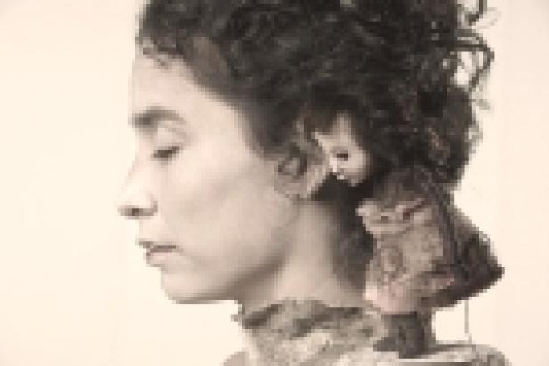 Das Profil einer Frau mit geschlossenen Augen, neben ihr eine kleine Puppe.