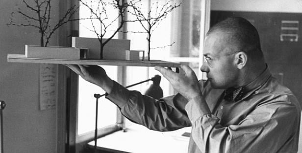 Ein Architekt betrachtet ein Modell eines Hauses mit Bäumen.