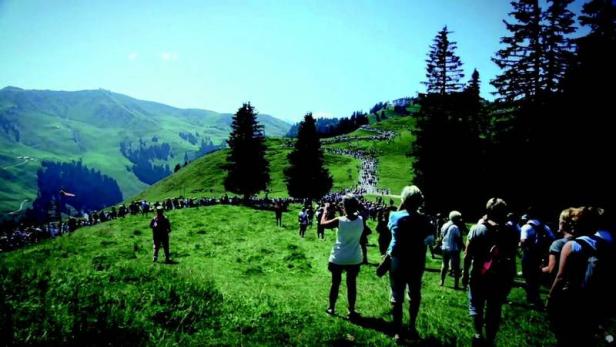 Eine Menschenmenge wandert auf einem grünen Hügel in Richtung eines Berges.