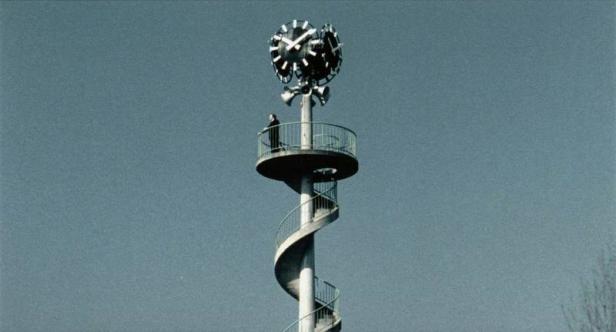 Ein hoher Turm mit einer Wendeltreppe und mehreren Uhren oben.