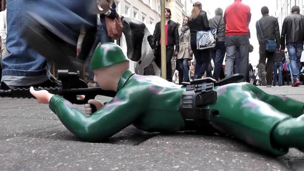 Ein Spielzeugsoldat liegt auf dem Bauch und zielt mit einem Gewehr auf der Straße.