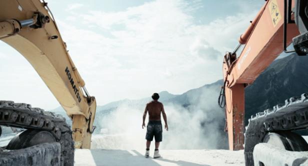 Ein Mann steht zwischen zwei Baggern vor einer Bergkulisse.