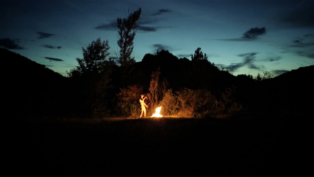 Eine Person steht nachts an einem Lagerfeuer.