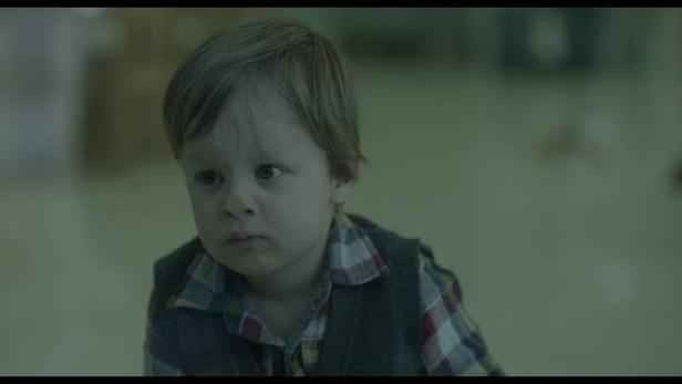 Ein kleiner Junge mit blonden Haaren und kariertem Hemd schaut aufmerksam.