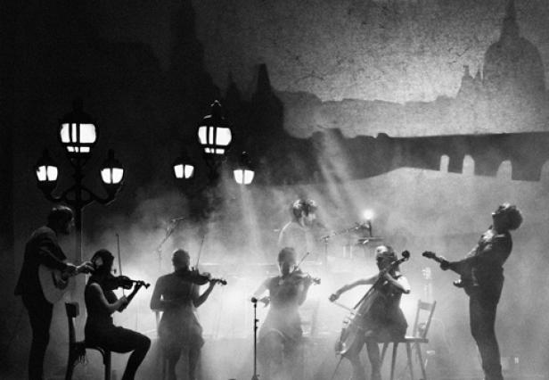 Eine Band spielt auf einer Bühne mit Straßenlaternen und einer gemalten Stadtkulisse im Hintergrund.