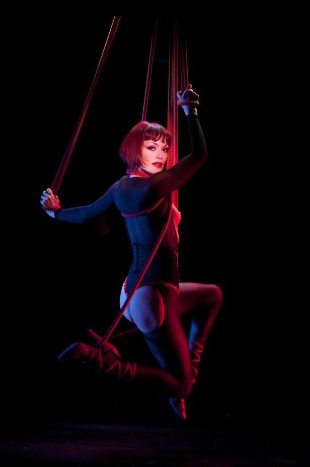 Eine Frau mit roten Haaren performt eine akrobatische Übung an roten Seilen.